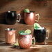 Three Arcoroc hammered black Moscow mule mugs with ice and lime on a counter.
