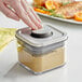 A person using an OXO Good Grips square plastic food storage container with a stainless steel lid to store food.