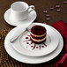 A plate of red velvet cake and a cup of coffee on a white porcelain plate with a Dresden International Tableware plate.