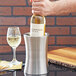 A person opening a bottle of wine in a stainless steel hourglass shape wine cooler.