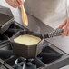 A person stirring soup in a Finex cast iron sauce pan on a stove.