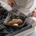 A person cooking a steak in a FINEX cast iron grill pan on a stove.