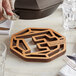 A cherry wood trivet with the FINEX logo on it under a wooden spoon on a table.
