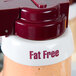 A close up of a white Tablecraft salad dressing dispenser collar with maroon lettering that says "Fat Free"