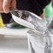 A person using a Vollrath stainless steel bar scoop to pour ice into a glass.