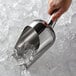 A hand holding a Vollrath stainless steel ice scoop filled with ice.