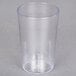 A Carlisle clear plastic tumbler on a gray surface with a straw in it.