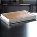 A rectangular white fiberglass sheet pan extender on a metal tray with brown substance inside.