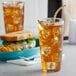 A Carlisle clear polycarbonate tumbler filled with ice tea on a table next to a sandwich.