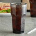 A Carlisle Louis smoke plastic tumbler filled with soda on a table with a sandwich.