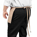 A man wearing a khaki Uncommon Chef waist apron with three pockets.