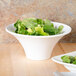 An American Metalcraft flared round melamine bowl filled with salad on a wooden table.