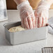 A person in plastic gloves putting dough into a Vollrath stainless steel bread loaf pan.