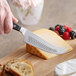 A hand holding a Wusthof Classic hard cheese knife cutting cheese.