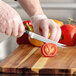 A person in gloves using a Wusthof Classic forged tomato knife to cut a tomato on a cutting board.