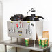 A Bunn stainless steel U3 twin coffee machine urn on a table with coffee cups and a dispenser.