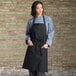 A woman wearing a black Uncommon Chef bib apron with three pockets.