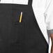 A person wearing a black Uncommon Chef bib apron with a pencil in the pocket.