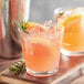 Two Acopa Select Old Fashioned glasses filled with pink lemonade, ice, and lemon slices with rosemary sprigs on a wooden surface.