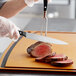 A person using a Wusthof carving knife to cut a piece of meat.