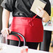 A woman wearing a red Uncommon Chef waist apron holding a book and pen.