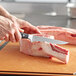 A person using a Wusthof Classic Ikon boning knife to cut meat on a cutting board.