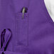 A purple Uncommon Chef bib apron with a pen in the pocket on a counter.