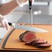A person using a Wusthof forged carving knife to cut meat on a cutting board.