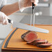 A person using a Wusthof Classic Forged Super Slicer to cut meat on a cutting board.