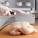 A person in gloves using a Wusthof Classic meat cleaver to cut a raw chicken on a cutting board.
