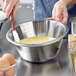 A person using a Linden Sweden stainless steel mixing bowl to mix yellow batter.