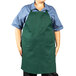 A man wearing a hunter green Uncommon Chef bib apron with three pockets.