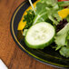 A Fineline Silver Splendor black plastic plate with gold bands holding a salad with cucumber and pepper.