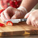 A person in gloves uses a Wusthof Classic Ikon forged paring knife to cut a strawberry on a cutting board.