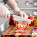 A person in gloves using a Wusthof Classic Nakiri knife to cut tomatoes on a cutting board.
