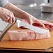 A person using a Wusthof Classic butcher knife to cut meat on a cutting board.