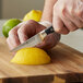A person's hands using a Wusthof Classic serrated paring knife to slice a lemon.