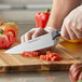 A person using a Wusthof Gourmet cook's knife to cut tomatoes on a cutting board.