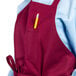 A person wearing a burgundy Uncommon Chef bib apron with a pencil in the pocket.