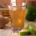 A Carlisle Alibi dessert shot glass filled with a brown liquid and lime wedges.