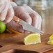 A person using an American Metalcraft bar knife to cut a lemon.