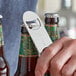 A hand using an American Metalcraft stainless steel flat bottle opener to open a bottle of beer.