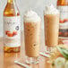 A bottle of Capora Sugar Free Caramel Flavoring syrup next to two glasses of iced coffee with whipped cream.