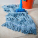A Carlisle blue wet mop with a blue headband on a tile floor.