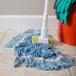 A Carlisle blue cotton blend wet mop with a yellow headband on the floor.