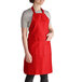 A woman wearing a red Intedge bib apron with pockets.