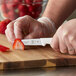 A person using a Mercer Culinary Ultimate White paring knife to cut a strawberry on a cutting board.