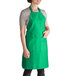 A woman wearing a Kelly green Intedge bib apron with pockets.