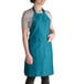 A woman wearing a teal Intedge bib apron with pockets.