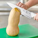 A person using a Mercer Culinary Ultimate White Chef Knife to cut a squash.
